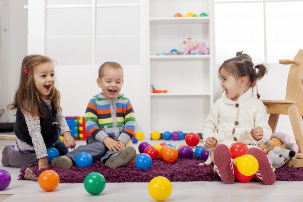 three children laughing together as they play with plastic balls.